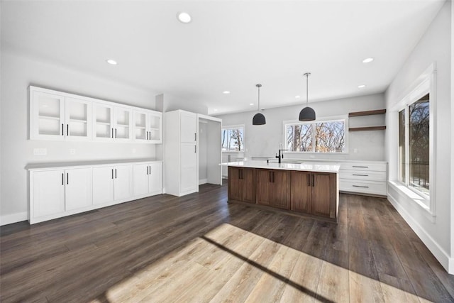 kitchen with a kitchen island with sink, pendant lighting, dark hardwood / wood-style floors, sink, and white cabinetry