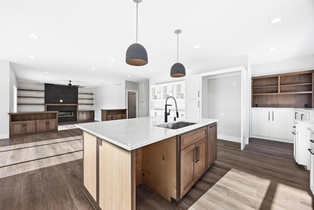 kitchen with sink, white cabinetry, a large fireplace, hanging light fixtures, and a center island with sink