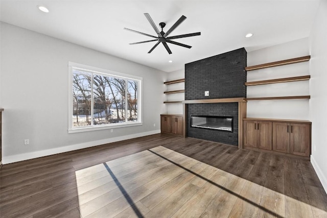 unfurnished living room featuring a fireplace, ceiling fan, and dark hardwood / wood-style floors