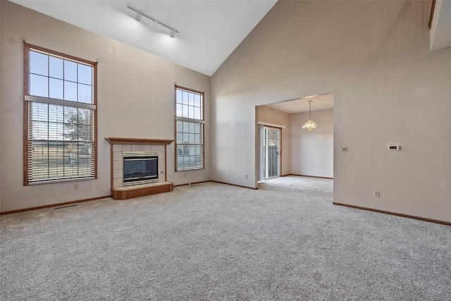 unfurnished living room featuring high vaulted ceiling, a tiled fireplace, a notable chandelier, and light colored carpet