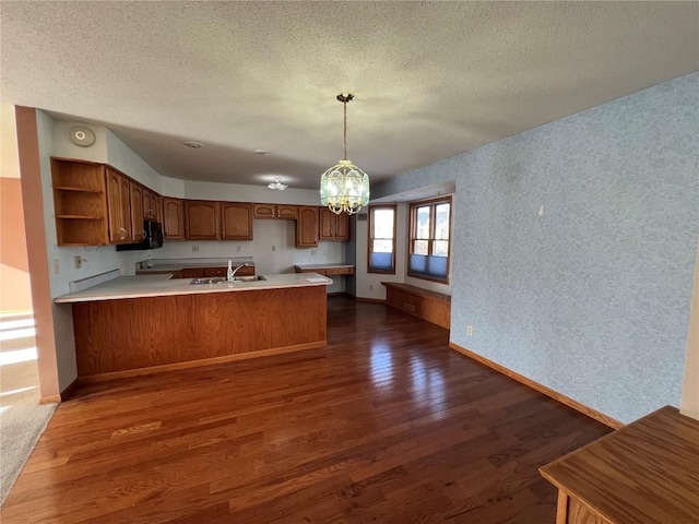 kitchen featuring kitchen peninsula, dark wood-type flooring, pendant lighting, a notable chandelier, and sink