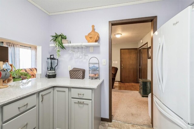 kitchen featuring light stone counters, light carpet, white fridge, and gray cabinetry