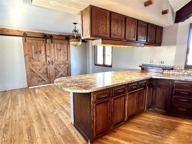 kitchen featuring light stone counters, light wood-type flooring, a barn door, and kitchen peninsula