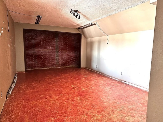 additional living space with lofted ceiling, brick wall, and a textured ceiling