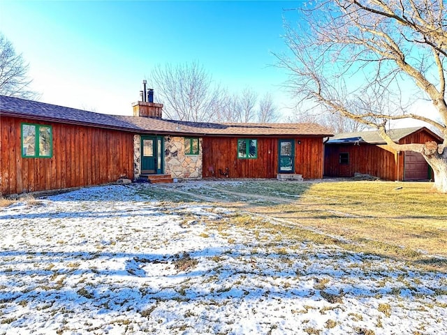 snow covered back of property with a lawn and a garage