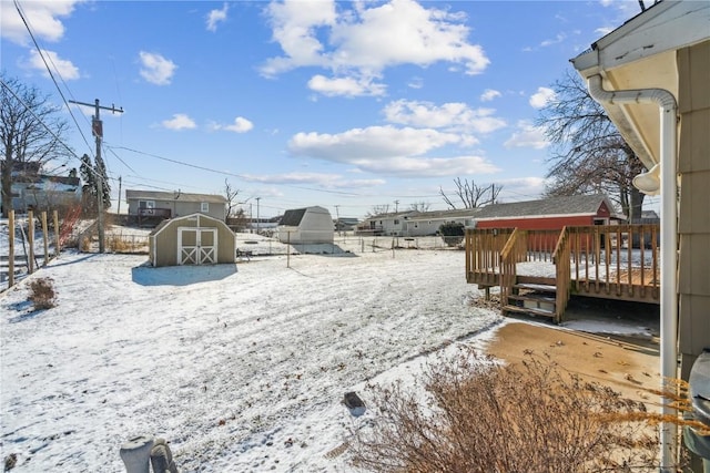 snowy yard with a storage shed and a wooden deck