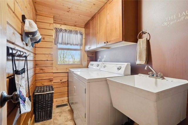 clothes washing area featuring cabinets, sink, independent washer and dryer, and wood walls