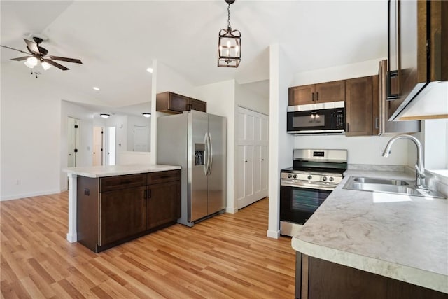 kitchen featuring stainless steel appliances, light wood-type flooring, ceiling fan, sink, and decorative light fixtures