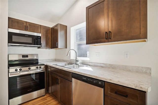 kitchen featuring sink, light hardwood / wood-style floors, dark brown cabinets, light stone countertops, and appliances with stainless steel finishes