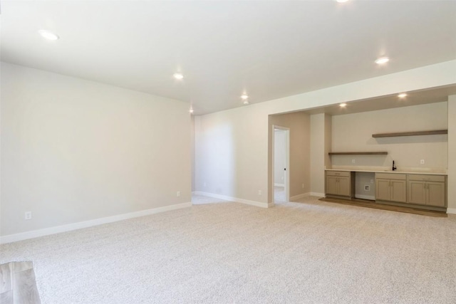 unfurnished living room with built in desk, light colored carpet, and sink