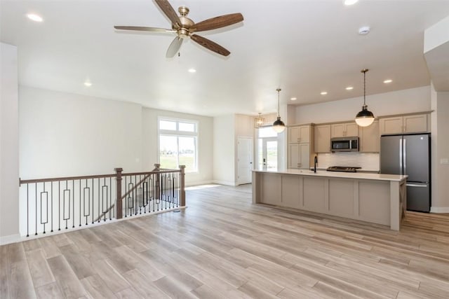 kitchen featuring stainless steel appliances, a kitchen island with sink, light hardwood / wood-style floors, and hanging light fixtures