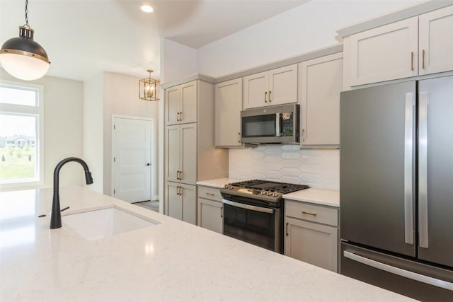 kitchen featuring appliances with stainless steel finishes, hanging light fixtures, light stone counters, and sink