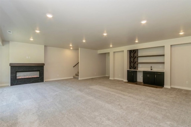 unfurnished living room with a premium fireplace, indoor bar, and light colored carpet