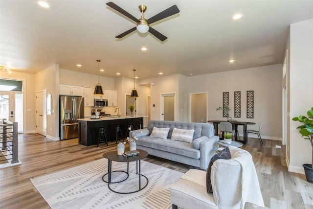 living room featuring light wood-type flooring, ceiling fan, and sink