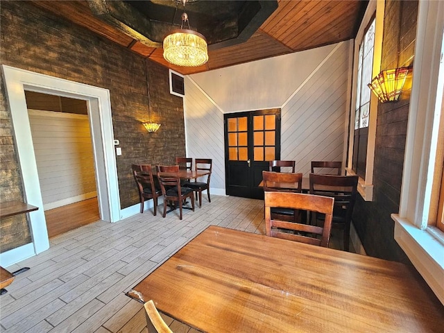 dining space featuring an inviting chandelier, french doors, wooden walls, and wooden ceiling