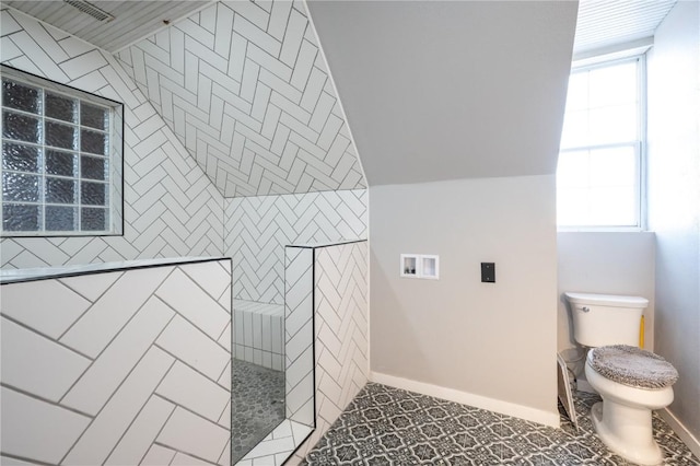 bathroom featuring toilet, tiled shower, and lofted ceiling