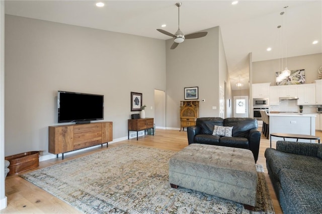 living room with high vaulted ceiling, light wood finished floors, and baseboards