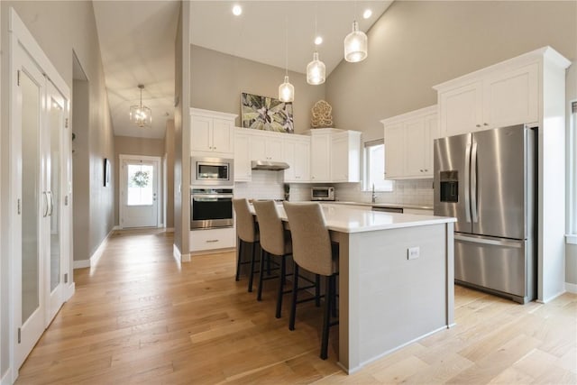 kitchen with a high ceiling, a center island, appliances with stainless steel finishes, and white cabinetry