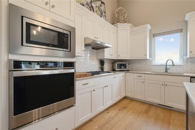 kitchen featuring appliances with stainless steel finishes, white cabinetry, decorative backsplash, and sink