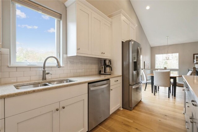 kitchen featuring vaulted ceiling, pendant lighting, stainless steel appliances, white cabinets, and sink