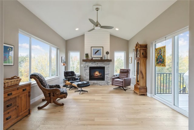 living area with lofted ceiling, ceiling fan, light hardwood / wood-style flooring, and a stone fireplace