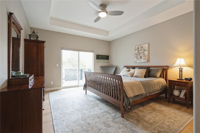 bedroom with ceiling fan, light hardwood / wood-style floors, access to outside, and a tray ceiling