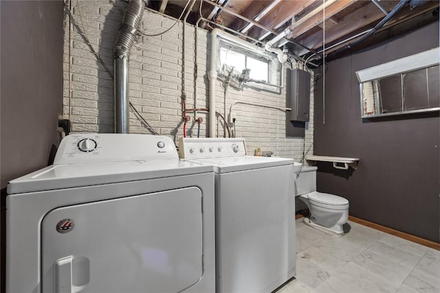 laundry area with electric panel, washer and clothes dryer, and brick wall