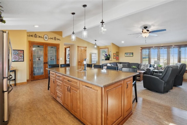 kitchen with light stone countertops, hanging light fixtures, stainless steel fridge, a kitchen island with sink, and light carpet