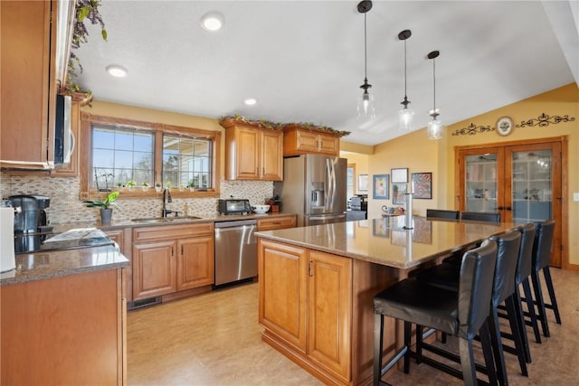 kitchen with vaulted ceiling, appliances with stainless steel finishes, a center island, sink, and decorative light fixtures