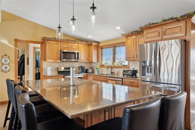 kitchen with vaulted ceiling, hanging light fixtures, a kitchen island, appliances with stainless steel finishes, and sink