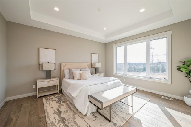 bedroom with wood-type flooring and a raised ceiling