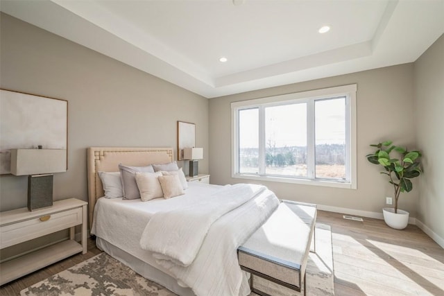 bedroom with light hardwood / wood-style flooring and a tray ceiling