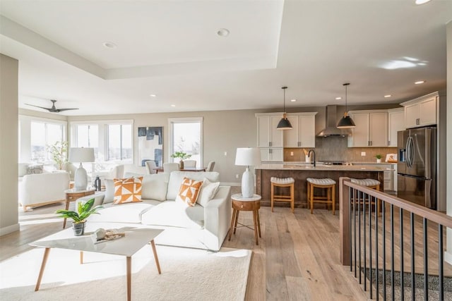 living room with a raised ceiling, ceiling fan, sink, and light hardwood / wood-style floors