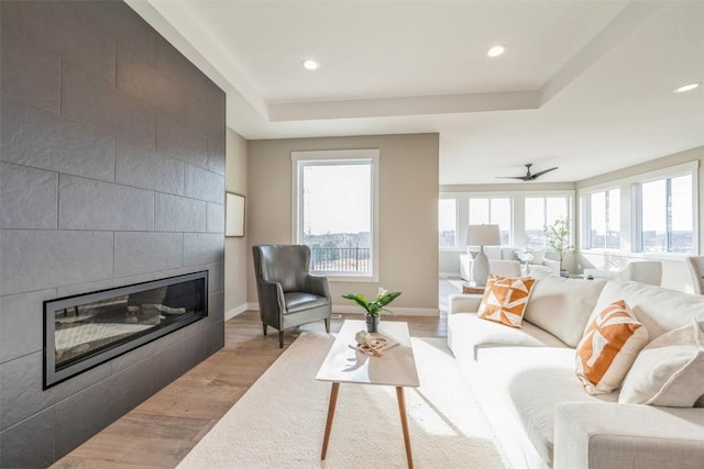 living room featuring ceiling fan, light hardwood / wood-style floors, a tray ceiling, and a tile fireplace