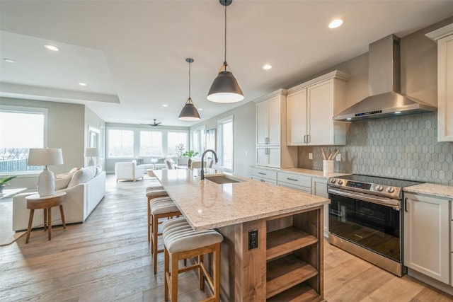 kitchen with stainless steel electric range oven, a center island with sink, light stone countertops, wall chimney exhaust hood, and sink