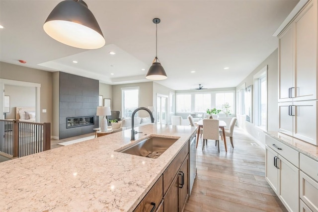 kitchen featuring ceiling fan, decorative light fixtures, light wood-type flooring, light stone counters, and sink