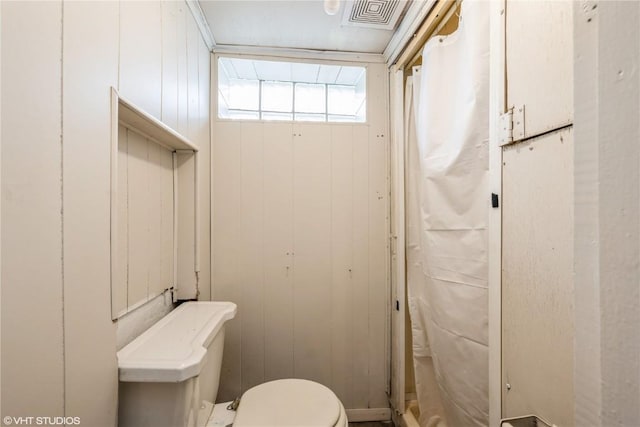 bathroom with toilet, crown molding, and wooden walls