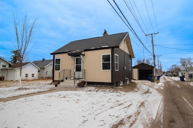 snow covered back of property with an outdoor structure and a garage