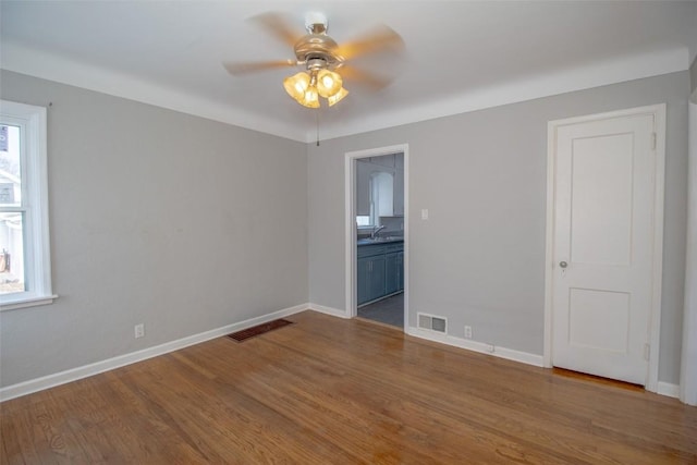 spare room with ceiling fan, sink, wood-type flooring, and a healthy amount of sunlight