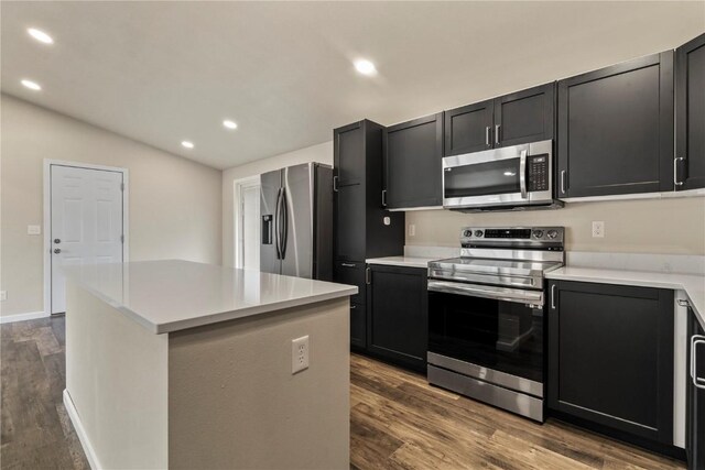 kitchen featuring dark wood-type flooring, a center island, stainless steel appliances, and vaulted ceiling