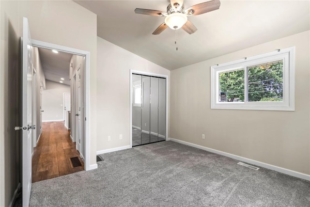 unfurnished bedroom featuring vaulted ceiling, dark carpet, ceiling fan, and a closet