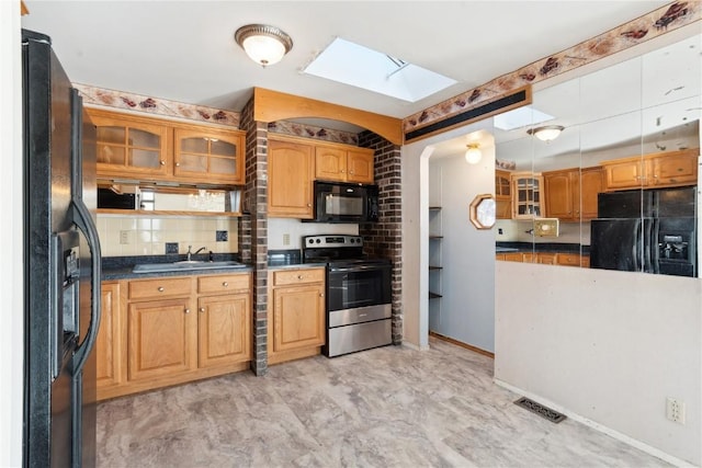 kitchen featuring decorative backsplash, sink, black appliances, and a skylight