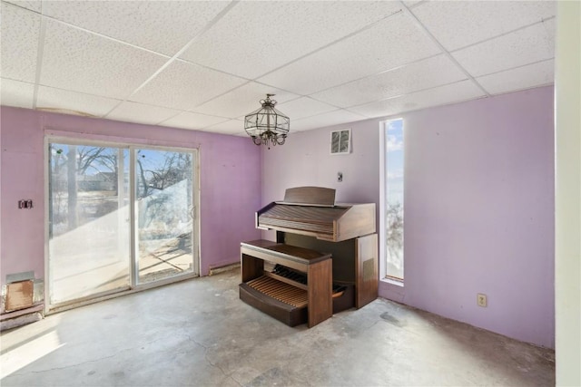 misc room with a paneled ceiling, an inviting chandelier, and concrete flooring