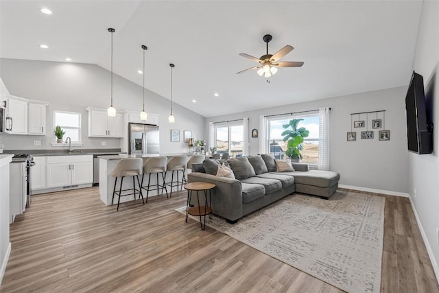 living room featuring ceiling fan, vaulted ceiling, sink, and light hardwood / wood-style flooring