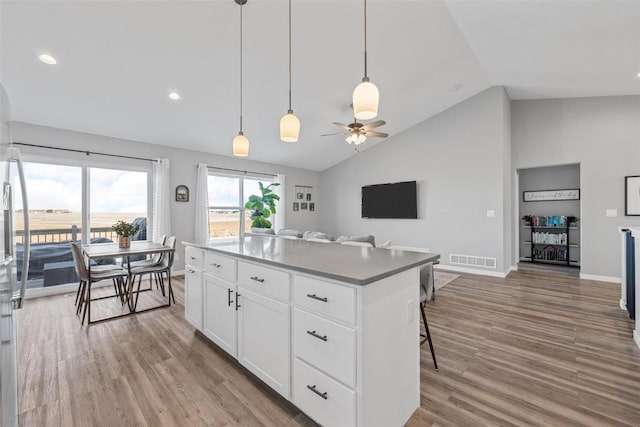 kitchen with light hardwood / wood-style floors, ceiling fan, vaulted ceiling, white cabinets, and a center island