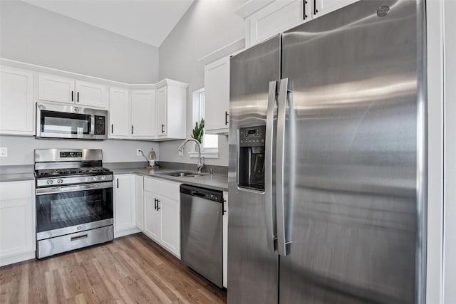 kitchen featuring appliances with stainless steel finishes, white cabinetry, sink, vaulted ceiling, and hardwood / wood-style flooring