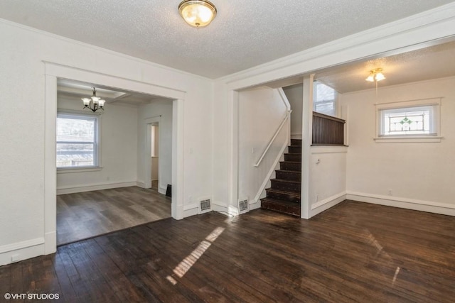 empty room featuring dark wood-type flooring, a textured ceiling, ornamental molding, and a healthy amount of sunlight