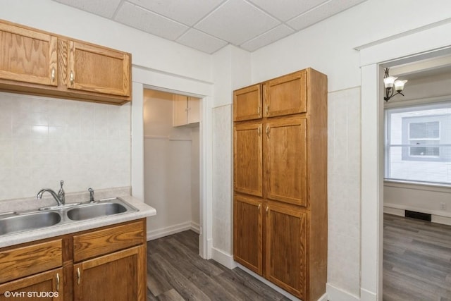 kitchen featuring dark wood-type flooring, decorative backsplash, sink, a chandelier, and a drop ceiling