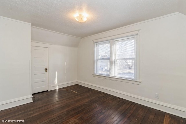 empty room with lofted ceiling, dark hardwood / wood-style floors, a textured ceiling, and ornamental molding