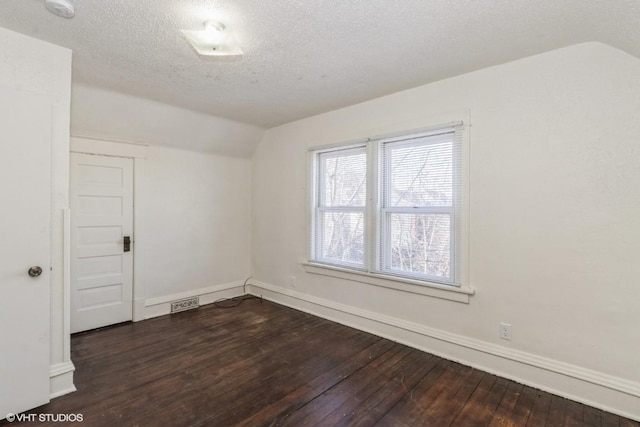 unfurnished room featuring a textured ceiling, dark hardwood / wood-style flooring, and vaulted ceiling